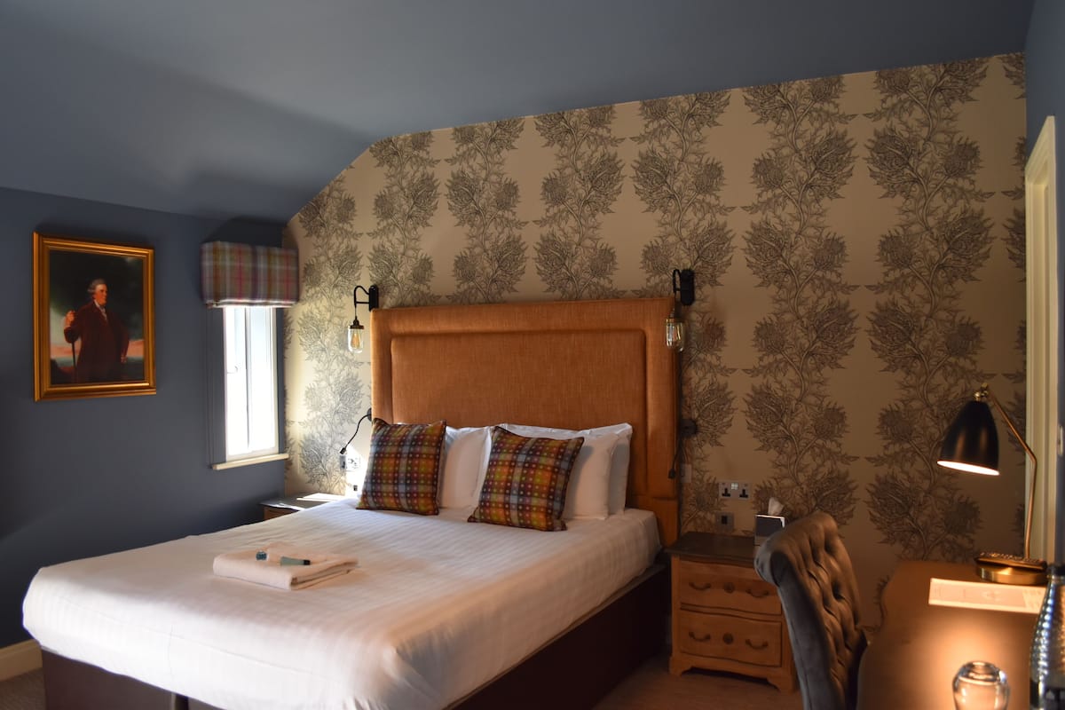A neatly made bed with a wooden headboard, a bedside table with a lamp, and a chair.