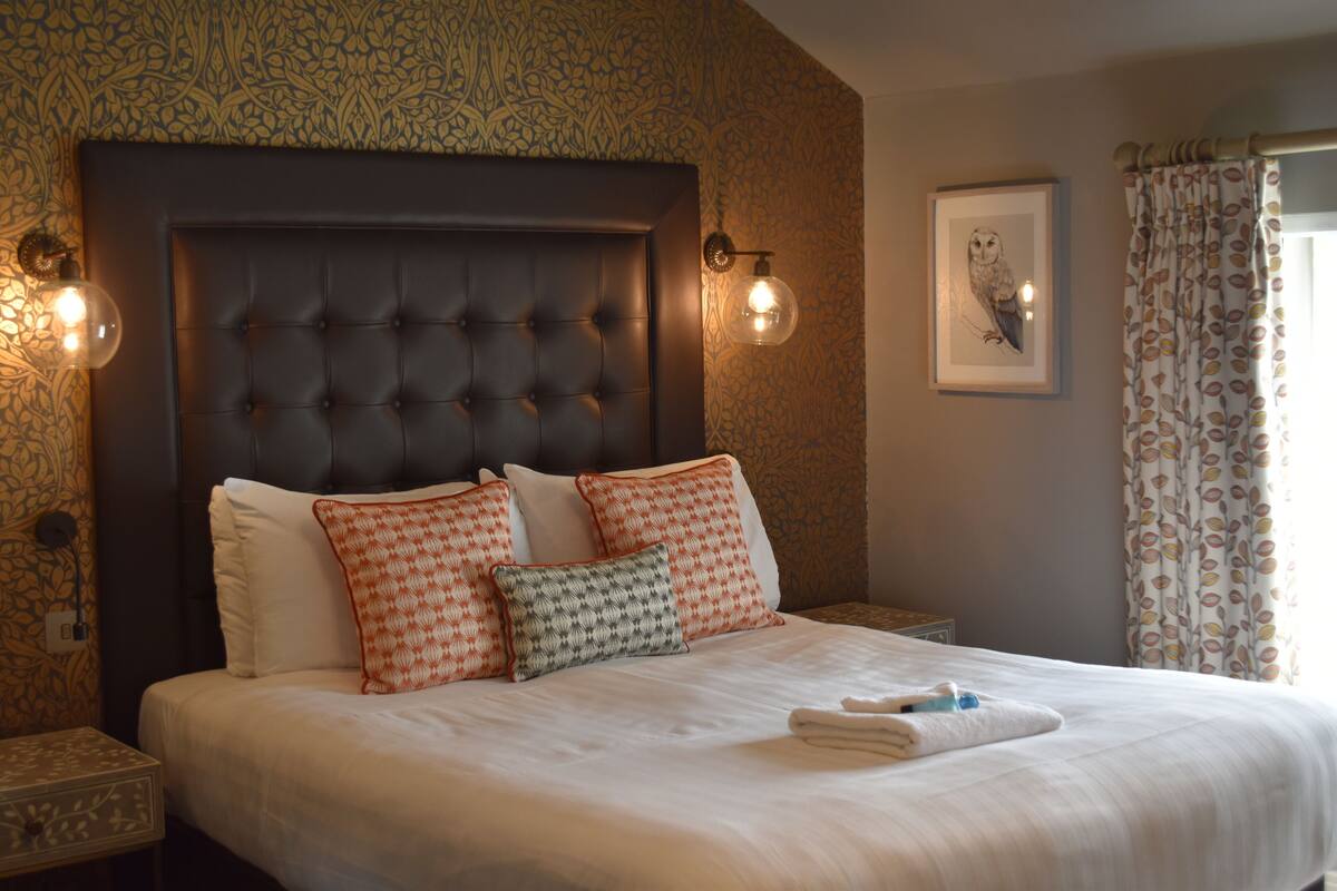 A neatly made bed with a tufted headboard, multiple pillows, and a framed artwork on the wall.