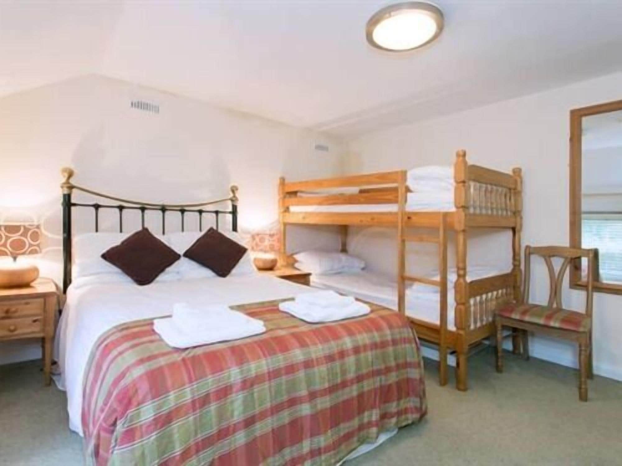 A bedroom with a single bed, a bunk bed, a chair, and a mirror.