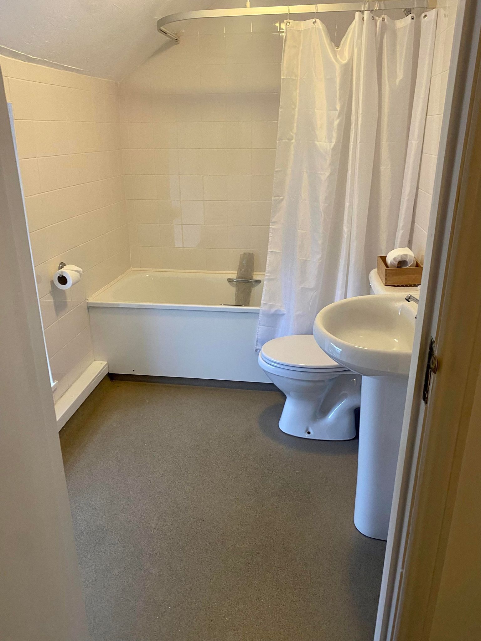 Un baño pequeño y limpio con una bañera blanca, inodoro y lavamanos.