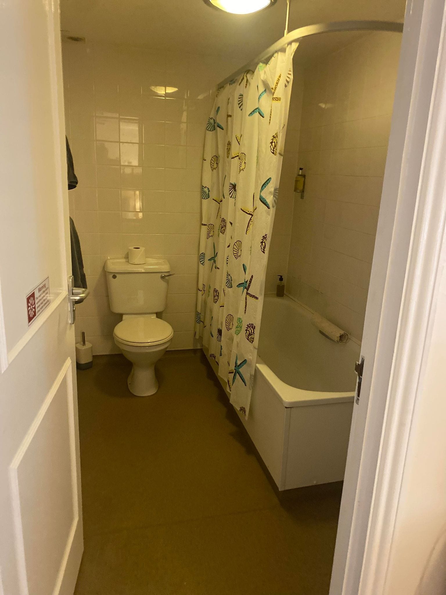 A bathroom with a toilet, a bathtub, and a shower curtain with a sea shell pattern.