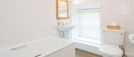 Un baño con bañera, inodoro, lavabo y ventana.
