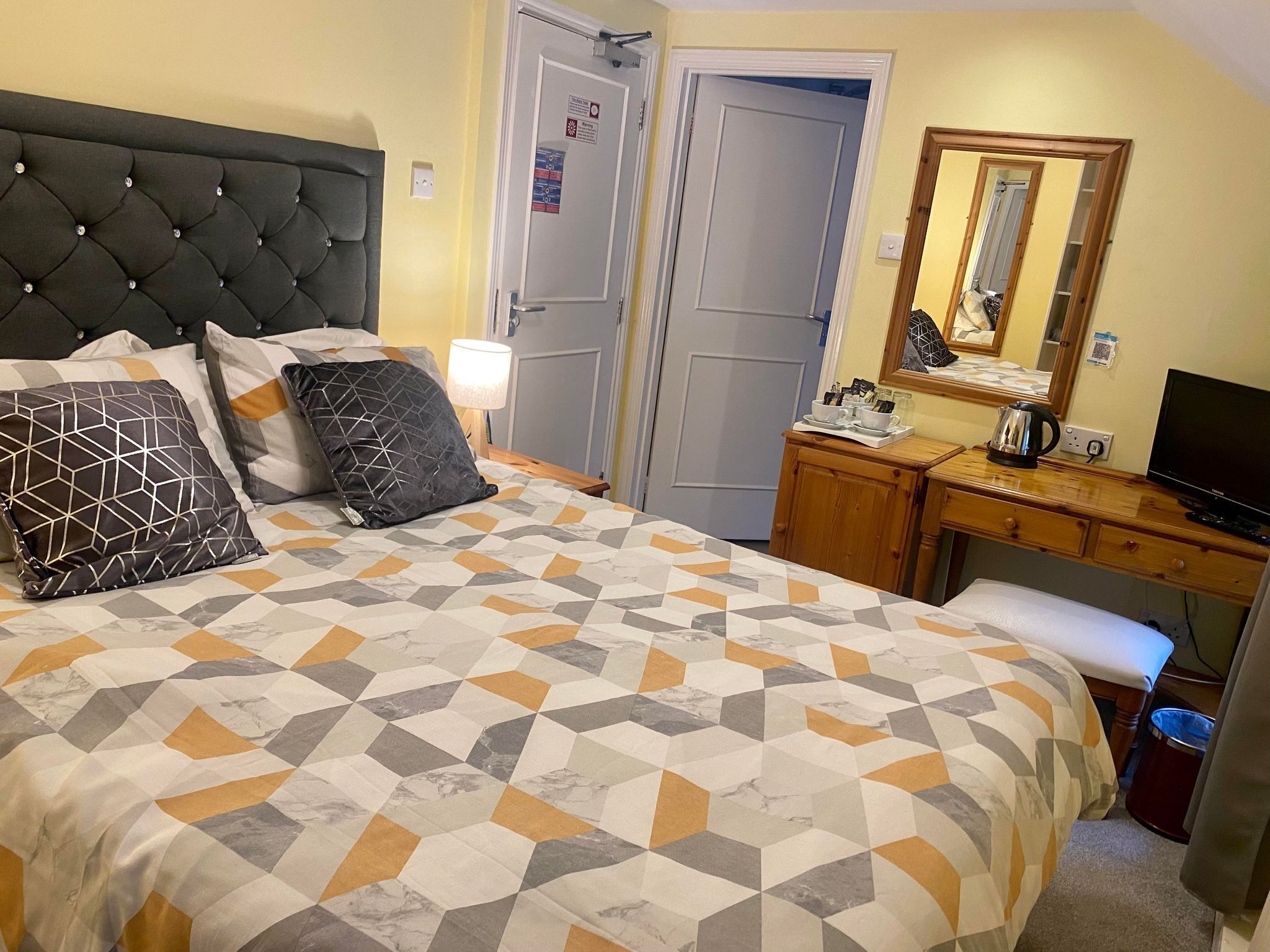 A neatly arranged bedroom with a bed, bedside table, dresser, and a mirror.