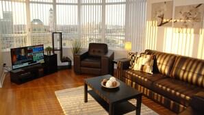 Una sala de estar moderna con un ventanal grande, un sofá de cuero, una mesa de centro y un televisor sobre un mueble.