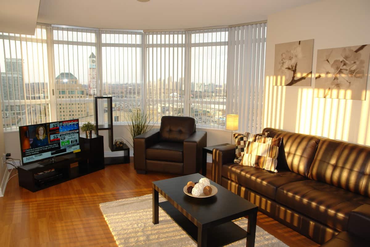 A modern living room with a large window, a leather sofa, a coffee table, and a TV on a stand.