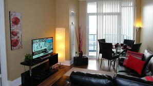 Una sala de estar con televisor, un sofá, una mesa de comedor con sillas y una ventana con persianas.