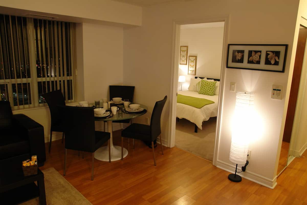 A compact living space with a dining area, a bed with green bedding, and a wall-mounted light fixture.