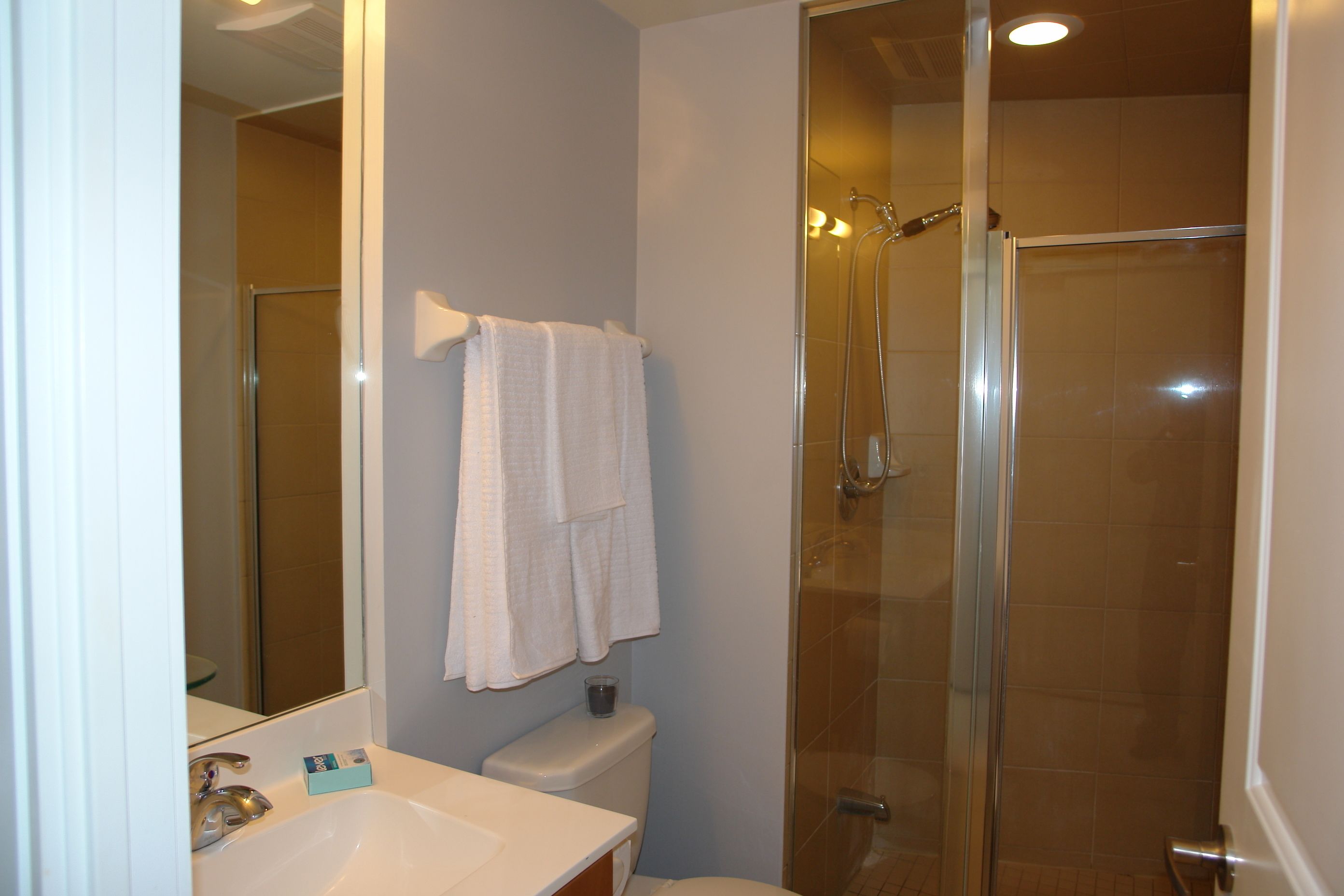 A bathroom with a glass-enclosed shower, a white sink, and a mirror.