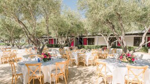 An outdoor dining area with round tables and chairs, surrounded by trees and buildings with red accents. - Hacienda de Leal,  BW Signature Collection (San Juan Bautista)