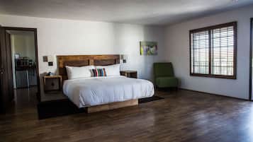 Ein Schlafzimmer mit einem hölzernen Bett, einem grünen Sessel, einem kleinen Tisch und einem Fenster mit Jalousien.