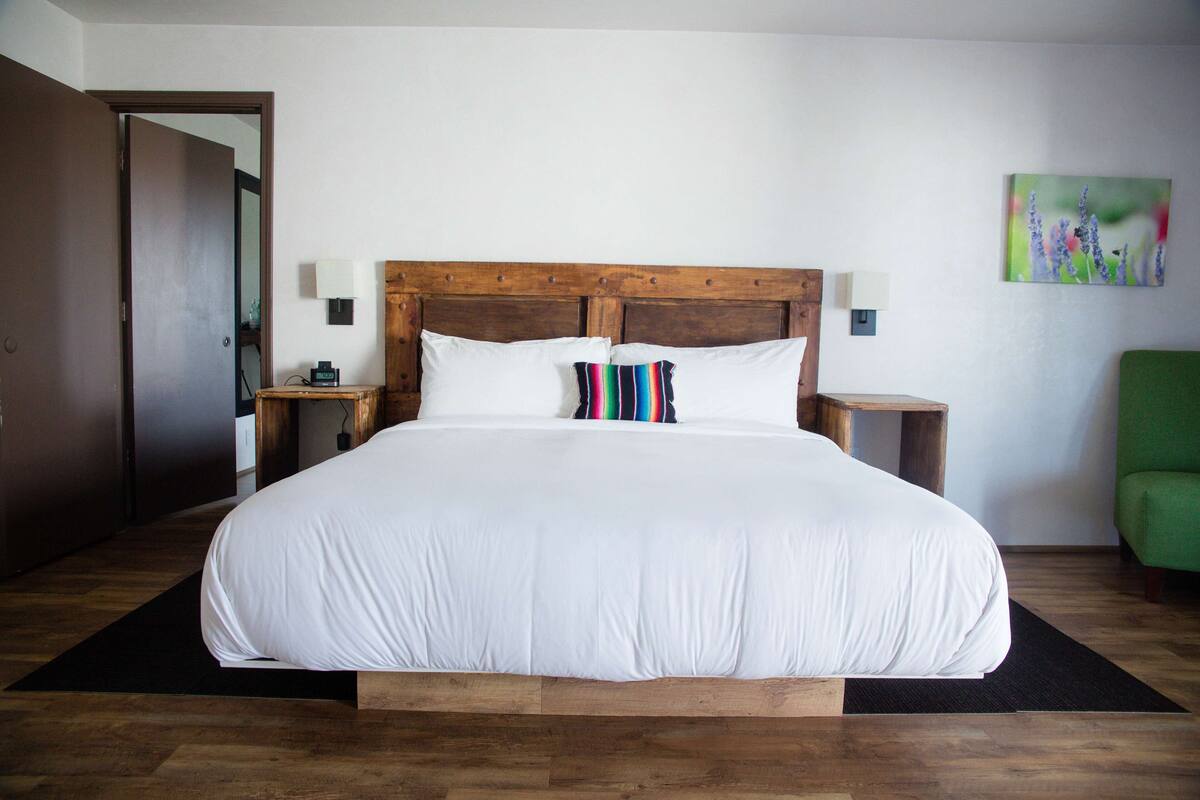 Ein großes Bett mit weißen Leinen, ein Holz-Kopfteil, zwei Nachttische mit Lampen und ein grüner Sessel.