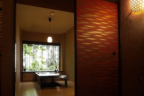 A room with a dining table, chairs, a hanging light fixture, and a large window with a view of trees. - Hana no kumo (Ito)