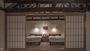 Quarto tradicional japonês com tatames, duas camas de madeira, um aparador de madeira baixo e uma porta de tela shoji.