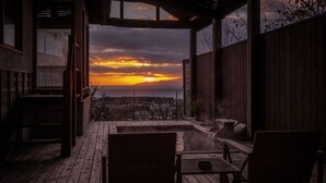 Um deck de madeira com hidromassagem e área de estar, com vista para um pôr do sol deslumbrante.