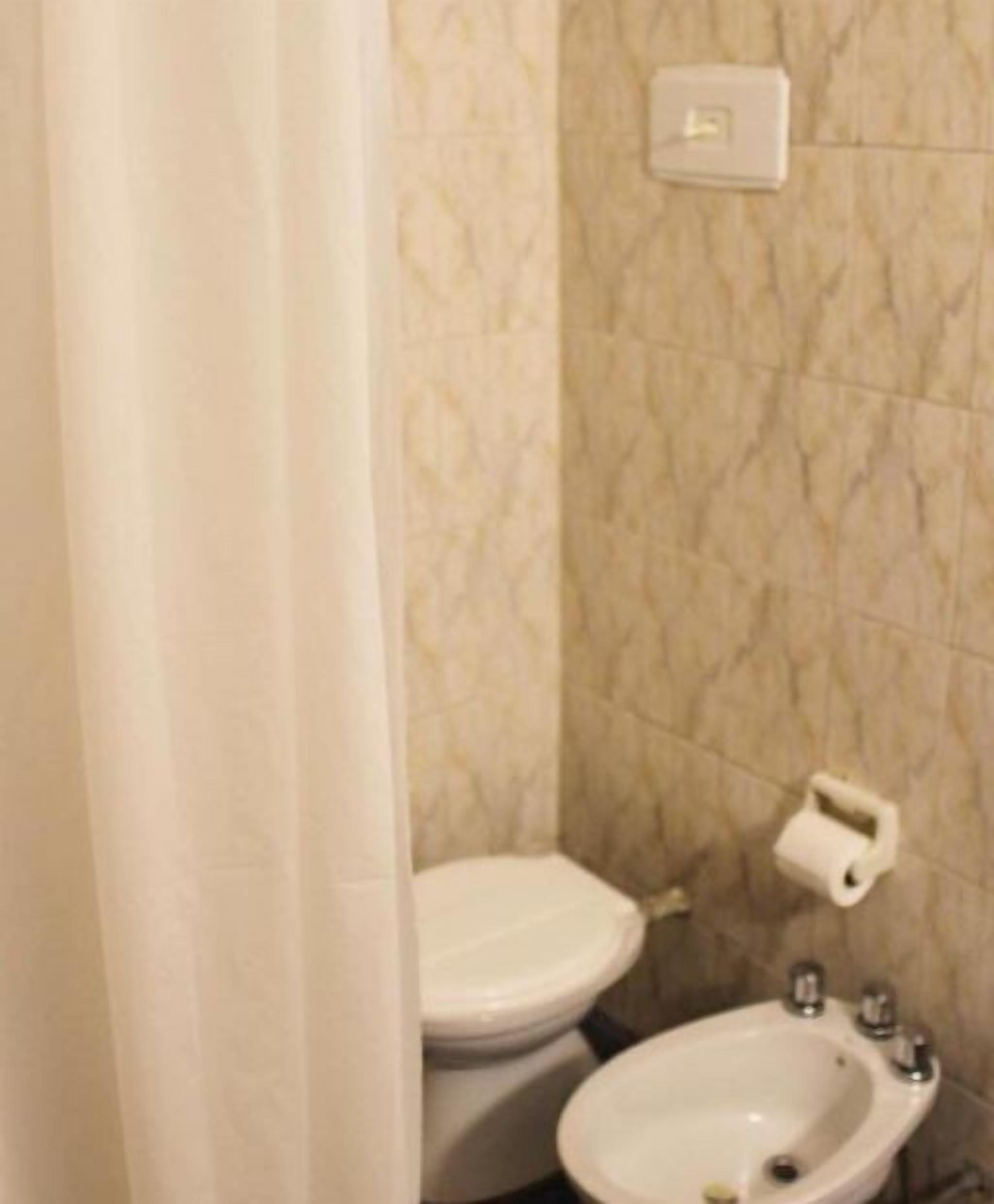 Un baño con inodoro, bidé y dispensador de papel higiénico en la pared.