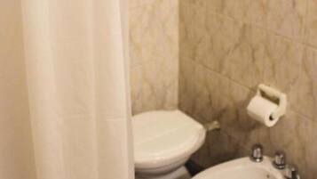 Un baño con inodoro, bidé y dispensador de papel higiénico en la pared.