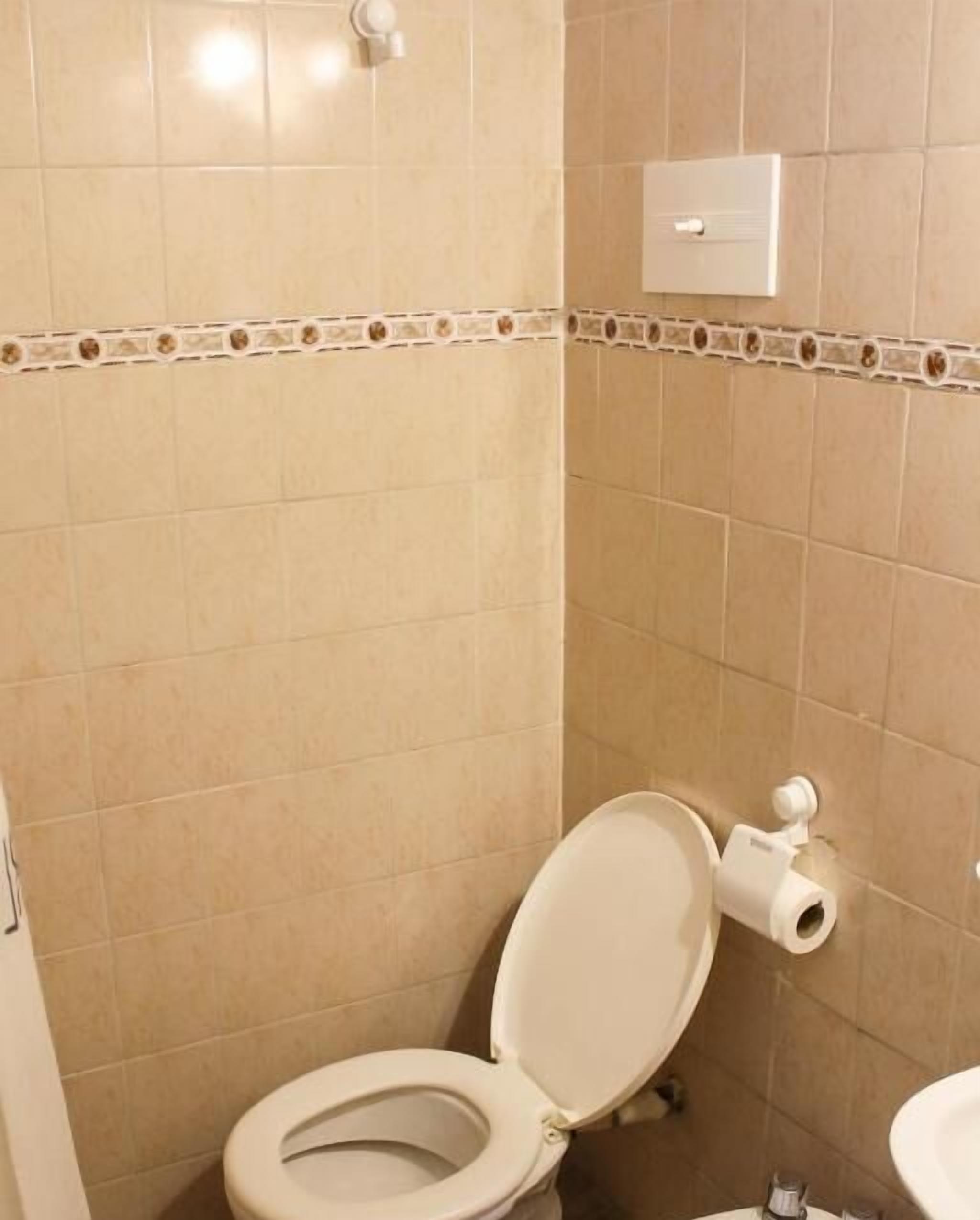 Un baño con inodoro, un dispensador de papel higiénico en la pared y suelo de baldosas.
