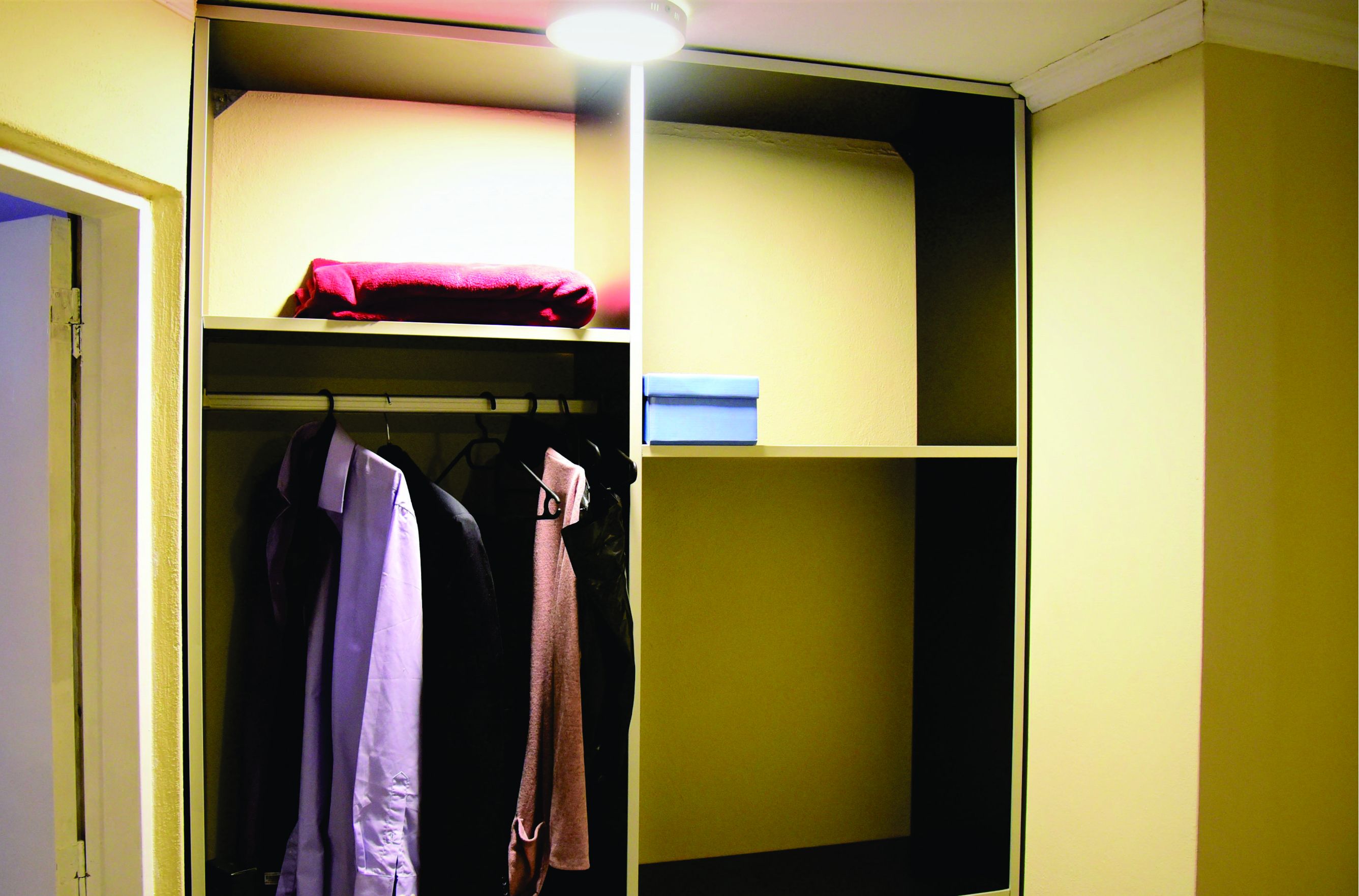 A dormitory room with a bunk bed, a wardrobe, and a hanging coat rack.