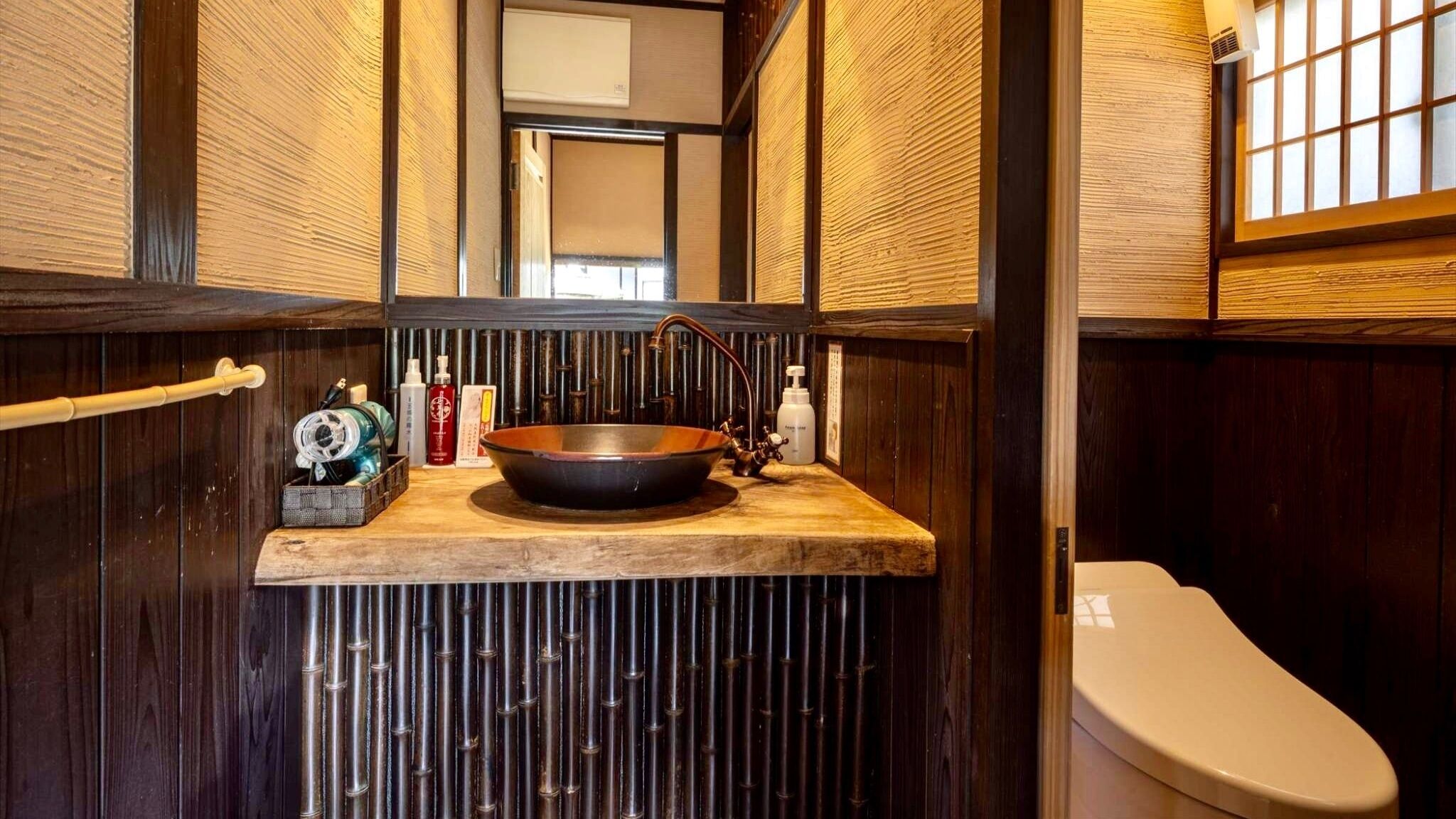 A bathroom with a wooden vanity, a copper sink, and a toilet.