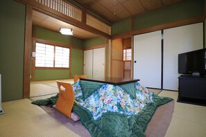 A traditional Japanese-style room with tatami flooring, a futon bed, sliding doors, and a television. - Makibanoie (Yufu)