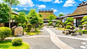 Un jardín japonés tradicional con senderos de piedra, rocallas y montañas al fondo.