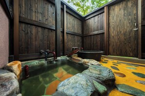 A traditional wooden bath area with a stone hot tub, wooden benches, and a yellow patterned floor. - Makibanoie (Yufu)