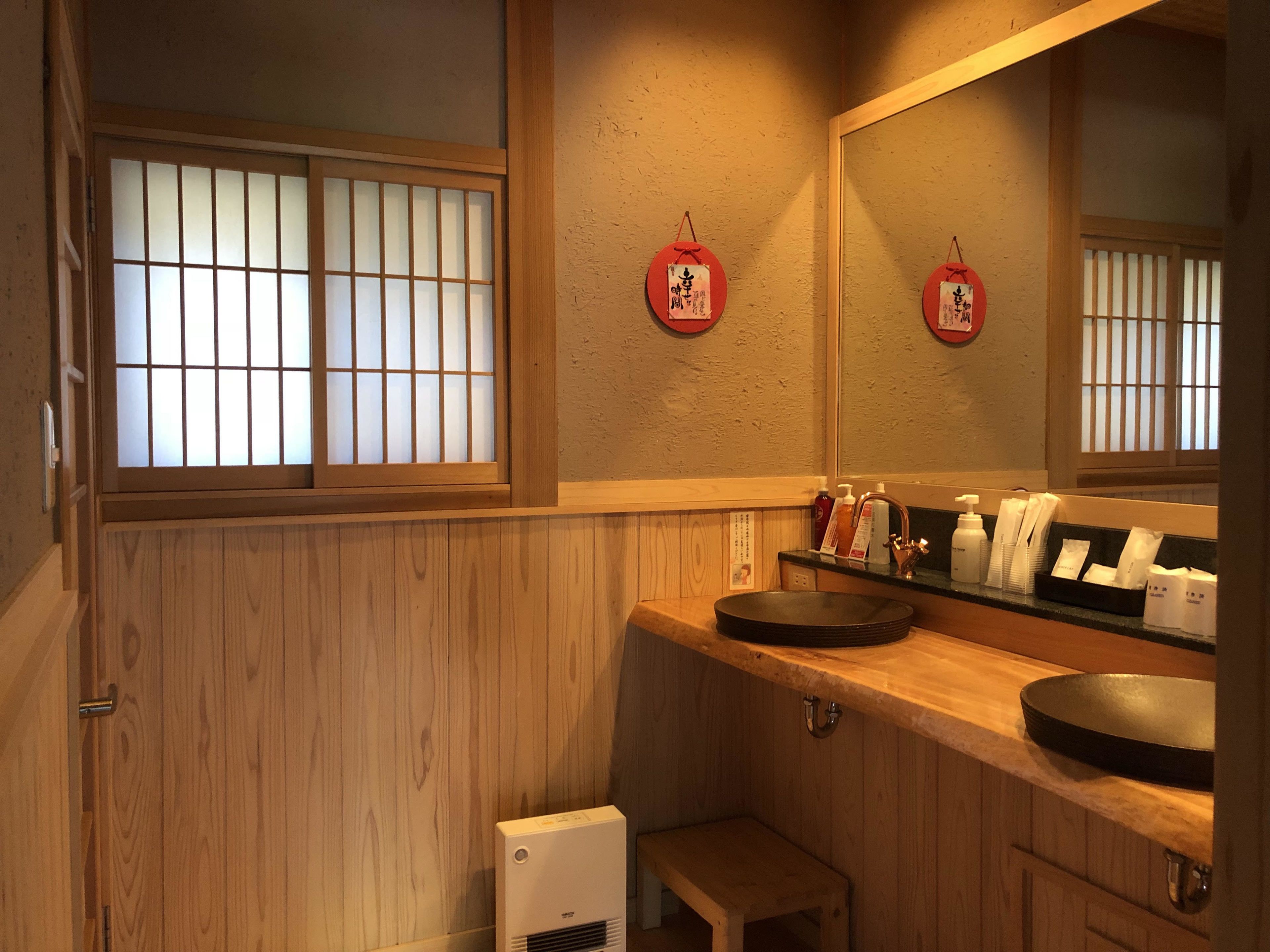 Ein traditionelles japanisches Badezimmer mit einem hölzernen Waschtisch, einem schwarzen Waschbecken und einem kleinen Hocker.