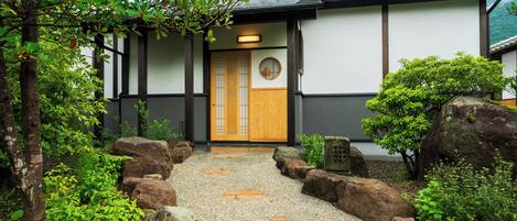 A traditional Japanese building with a wooden door, a stone pathway, and surrounding greenery.