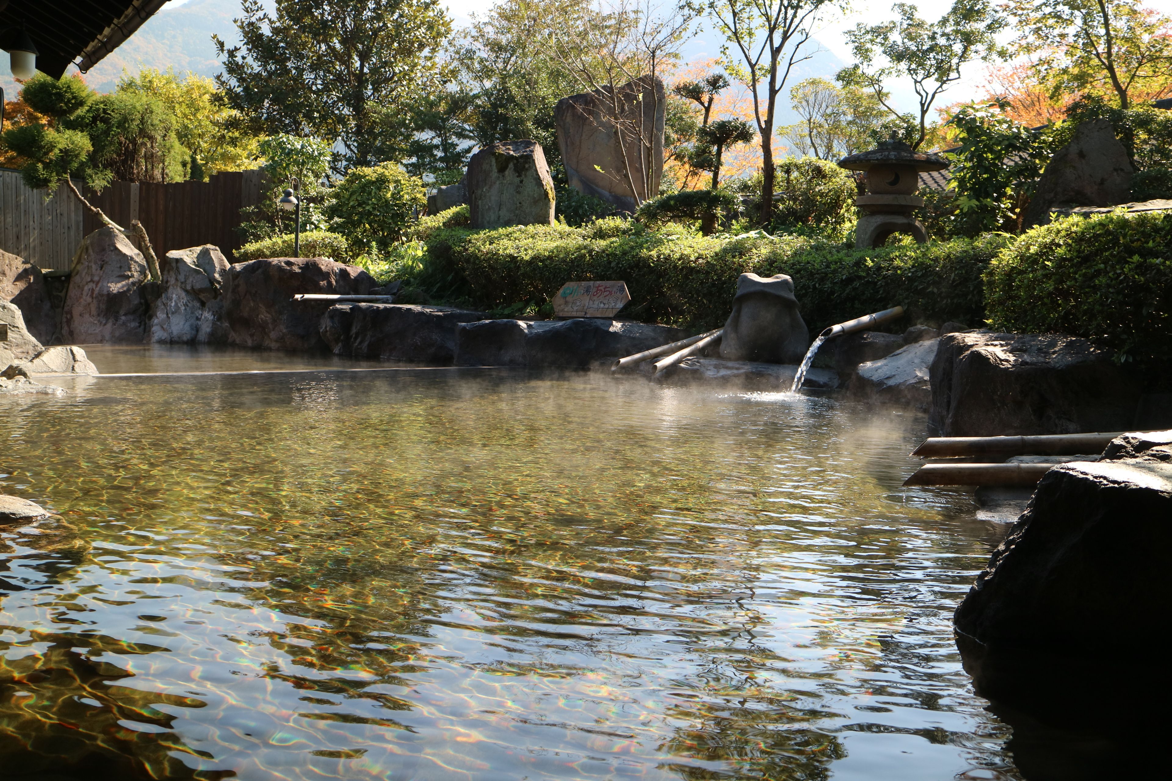 A tranquil outdoor setting with a clear water feature, rocks, and traditional architecture.