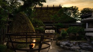 Un jardín japonés tradicional con un farol de piedra, un banco de madera y un edificio de estilo pagoda al fondo.