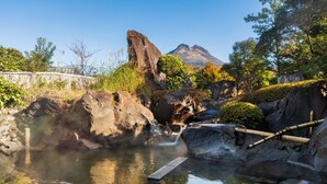 Un área de aguas termales con un pasillo de madera, rocas grandes y una montaña al fondo.
