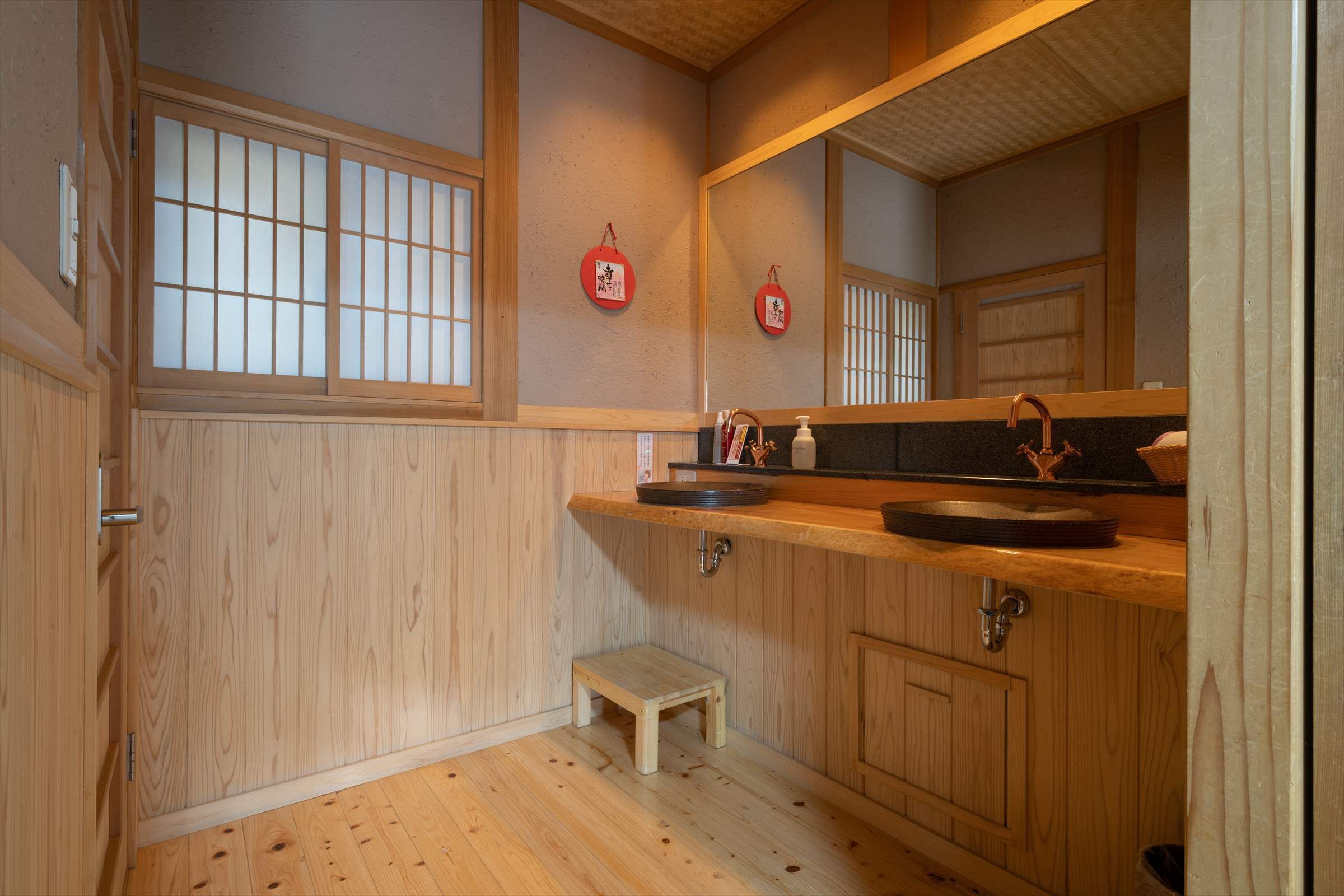 A traditional Japanese-style bathroom with wooden cabinetry, a small wooden stool, and a mirror.