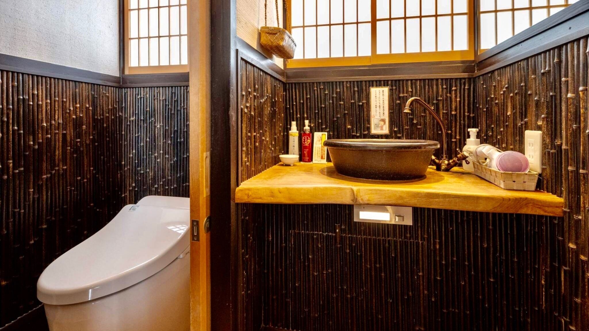 A traditional Japanese-style bathroom with a toilet, a sink with a large basin, and a bamboo wall.