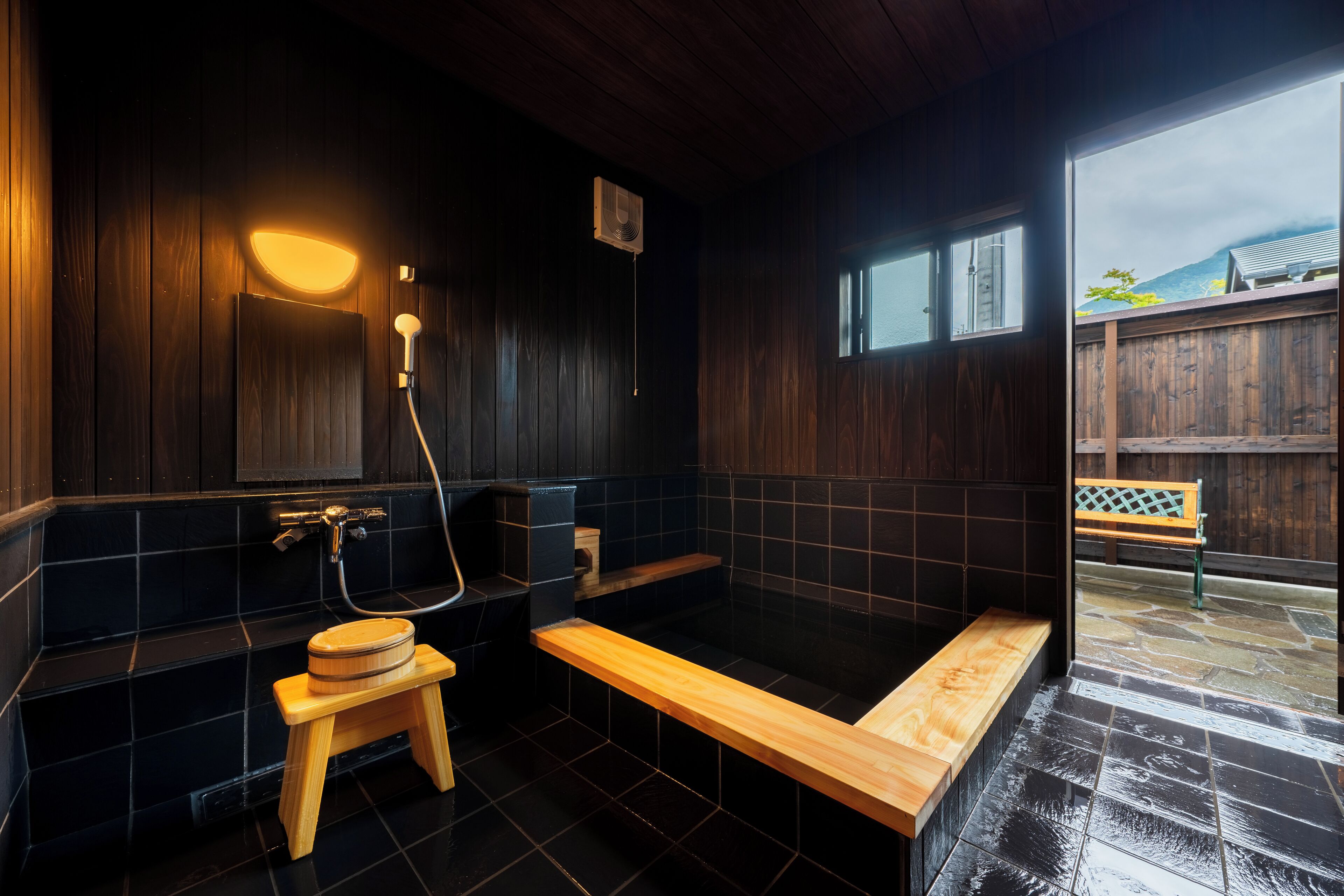 A modern bathroom with a wooden bench, a small stool, and a bathtub.