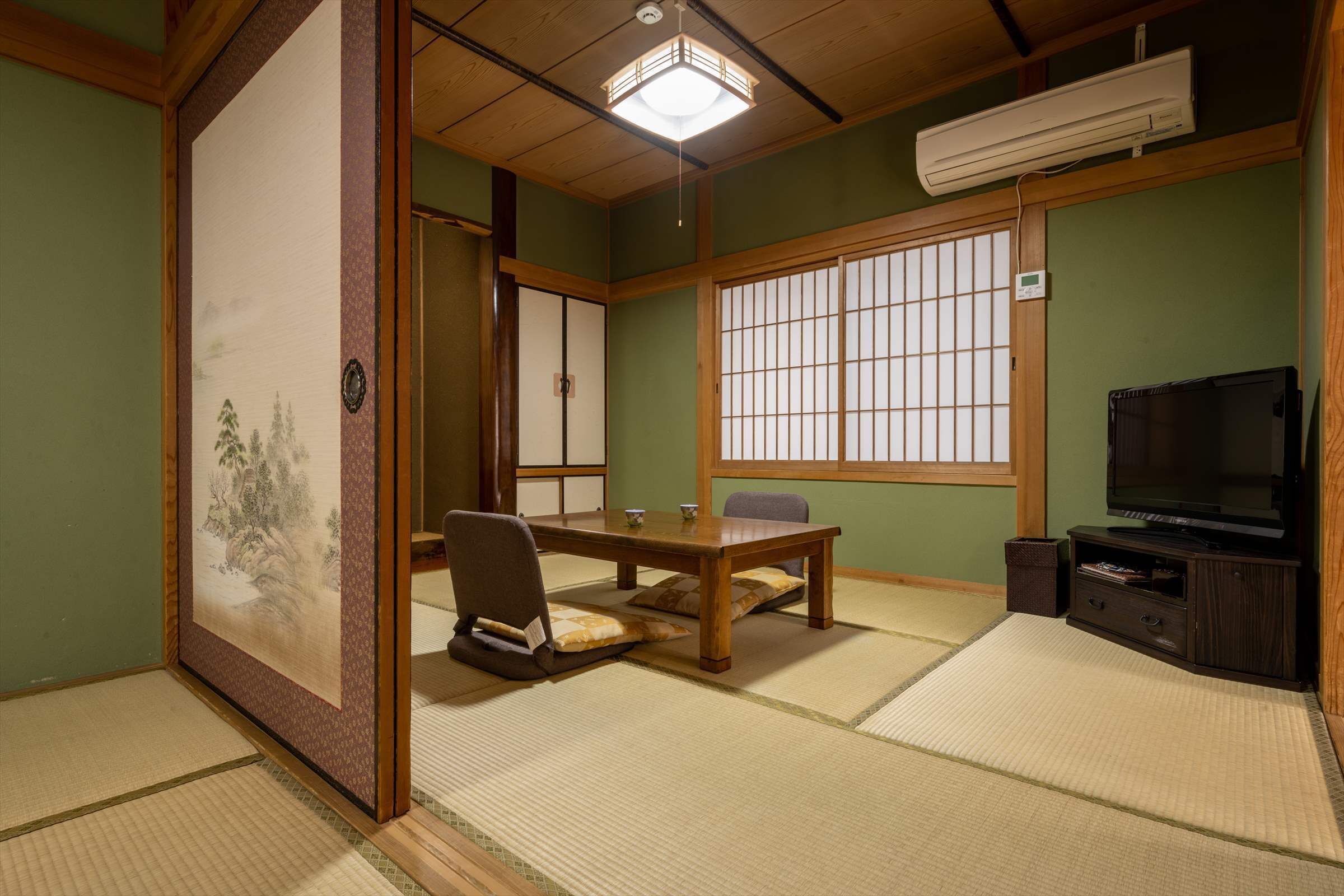 A traditional Japanese room with tatami flooring, a low table, a chair, a television, and a sliding door with a shoji screen.
