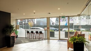 A hotel lobby with a reception desk, seating area, and large windows offering a view of the street. - Ramada Suites by Wyndham Christchurch City (Christchurch)