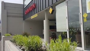 A modern building with a 'RAMADA' sign, a glass entrance, and a landscaped area with plants and rocks. - Ramada Suites by Wyndham Christchurch City (Christchurch)