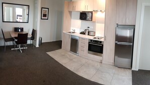 A modern kitchen with a microwave, oven, and refrigerator, a dining table with chairs, and a small trash can. - Ramada Suites by Wyndham Christchurch City (Christchurch)