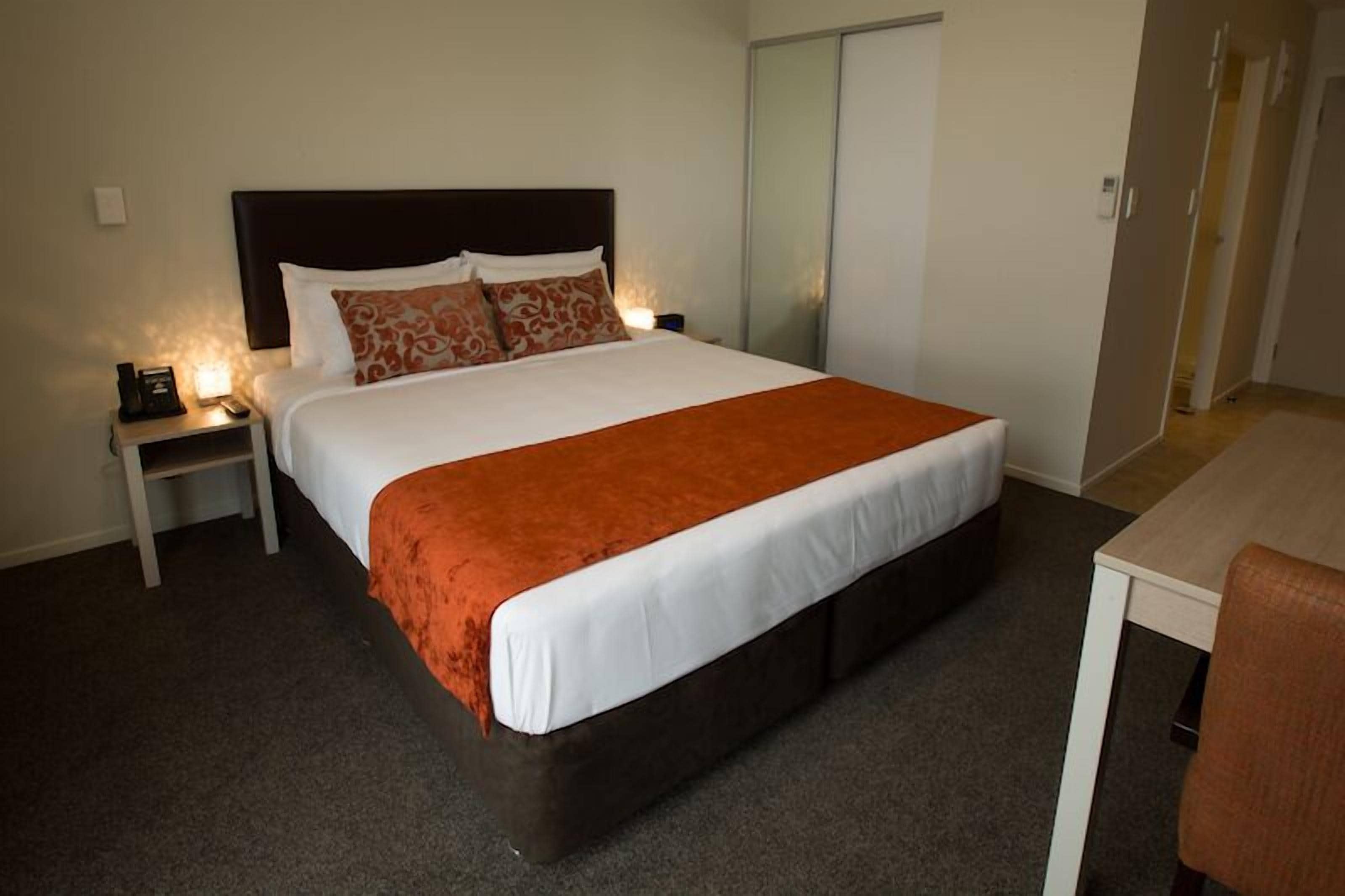A hotel room with a single bed, a bedside table with a lamp, and a desk with a chair.