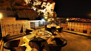 An outdoor dining area with tables and chairs, a view of a cliff, and a railing. - Has Cave Konak (Ürgüp)