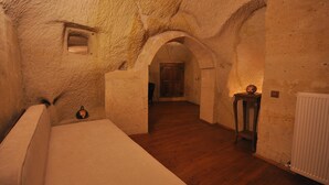 A cozy, vaulted room with a wooden floor, a cushioned bench, and a small table with a vase. - Has Cave Konak (Ürgüp)