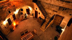 A courtyard with stone walls, a wooden staircase, and a table with chairs. - Has Cave Konak (Ürgüp)