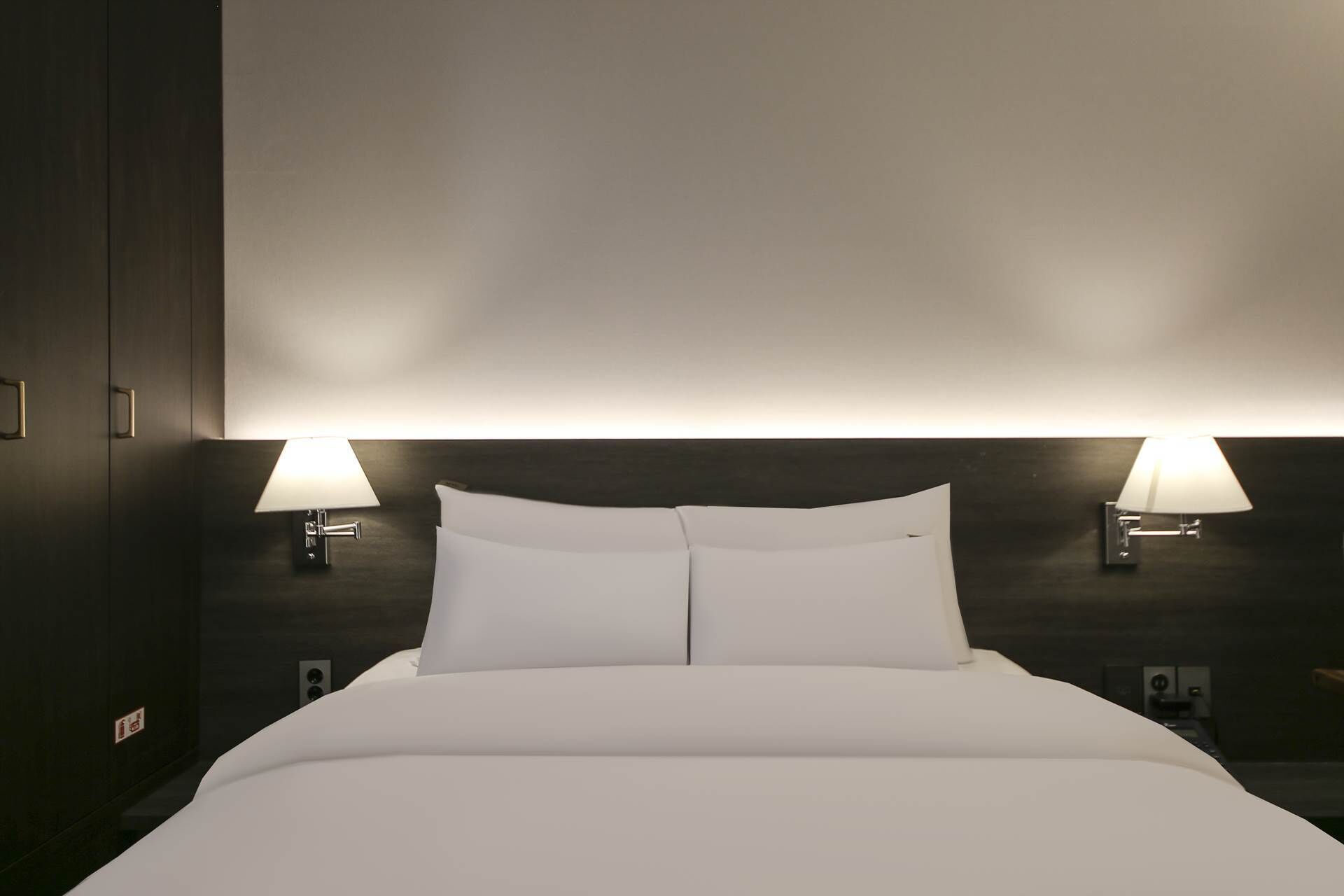 A hotel room with a large bed, two bedside lamps, and a dark wooden headboard.
