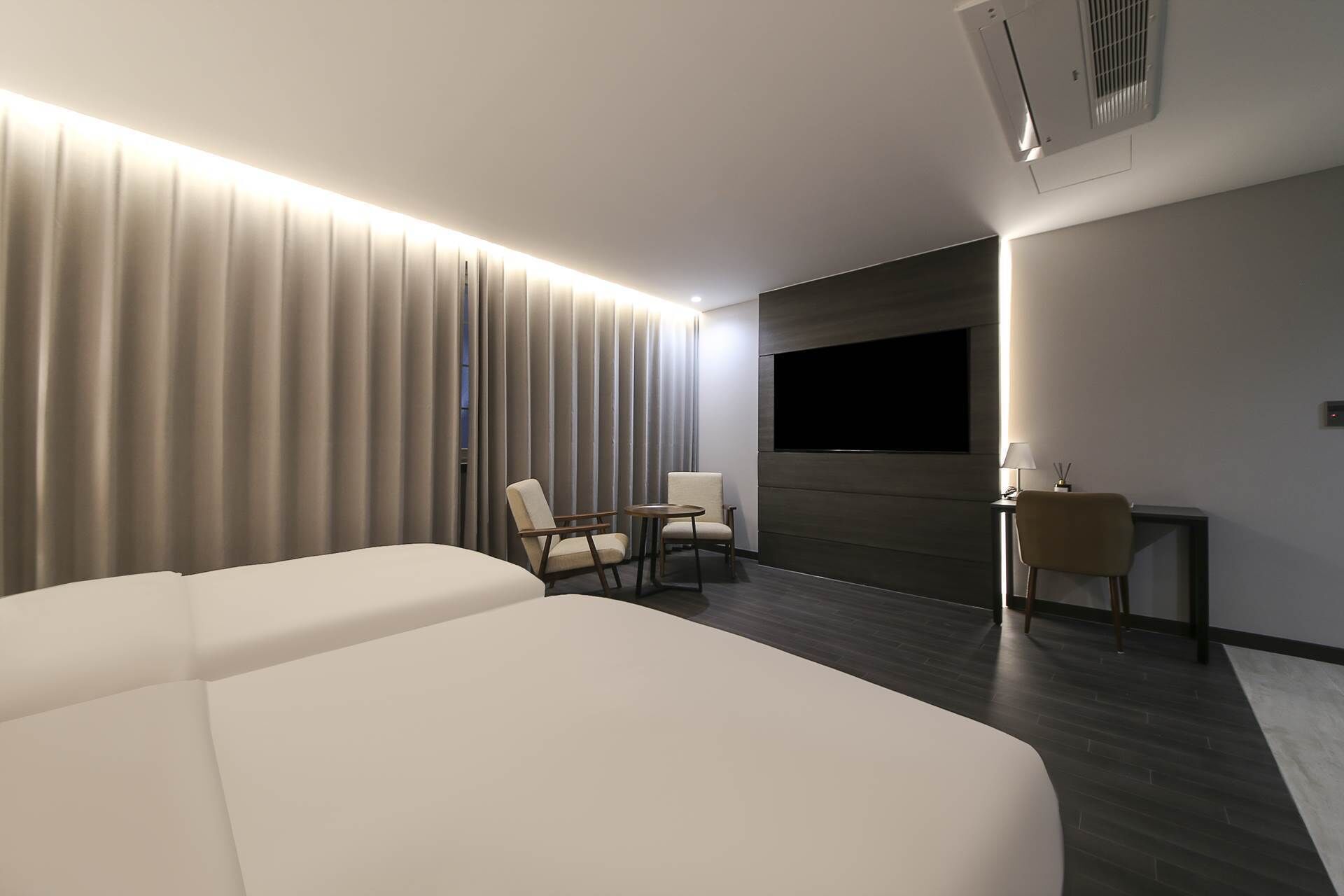 A modern hotel room with a large bed, two armchairs, a small table, and a TV mounted on the wall.