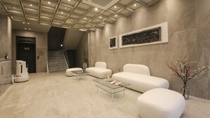 Un vestíbulo moderno con una escalera, sofás blancos, una mesa de centro de vidrio y obras de arte en las paredes.