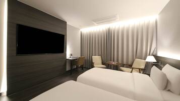 A modern hotel room with a large bed, a desk, two chairs, a TV, and a curtain backdrop.