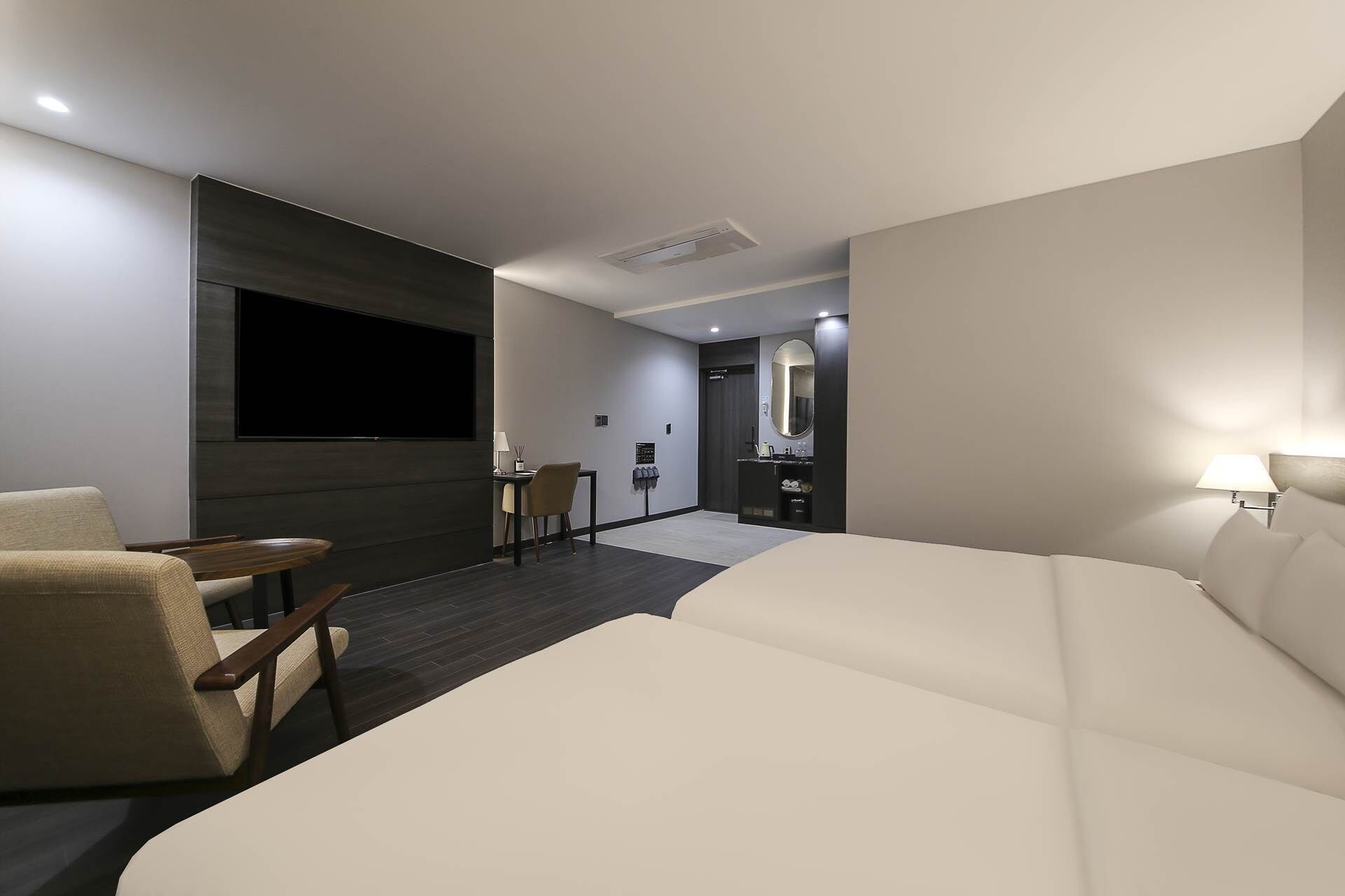 Una habitación de hotel moderna con una cama grande, un televisor de pantalla plana montado en la pared, un escritorio con una silla y una pequeña zona de estar con un sofá y sillones.