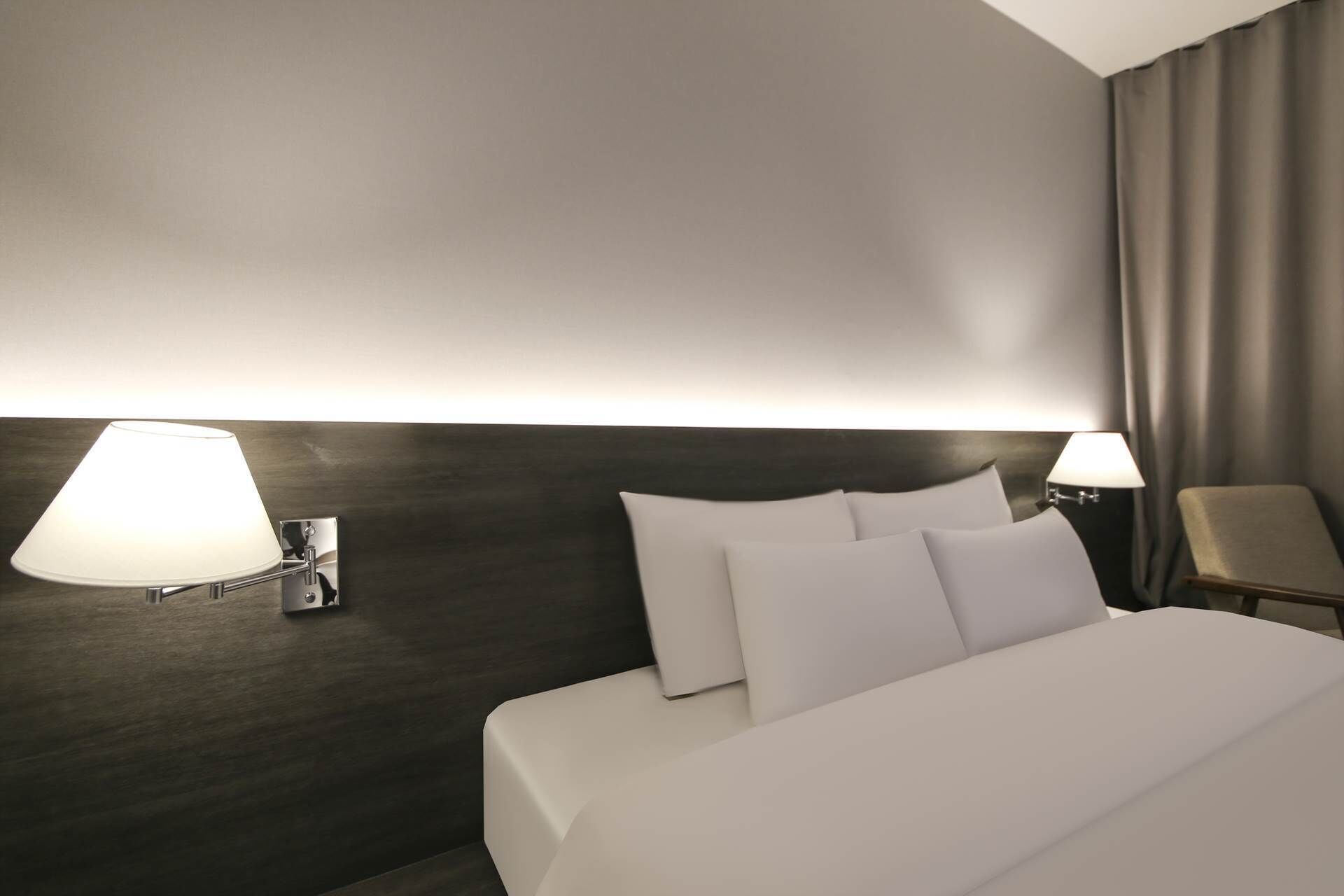 Una habitación de hotel con una cama grande, dos lámparas de pared y una silla.
