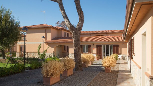 A building with a tiled roof, a paved walkway, and potted plants. - La Residenza del Golfo (Scarlino)
