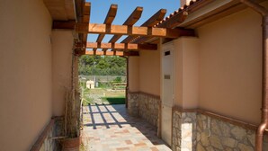 A corridor with a tiled floor, wooden pergola, stone walls, and a view of greenery in the distance. - La Residenza del Golfo (Scarlino)